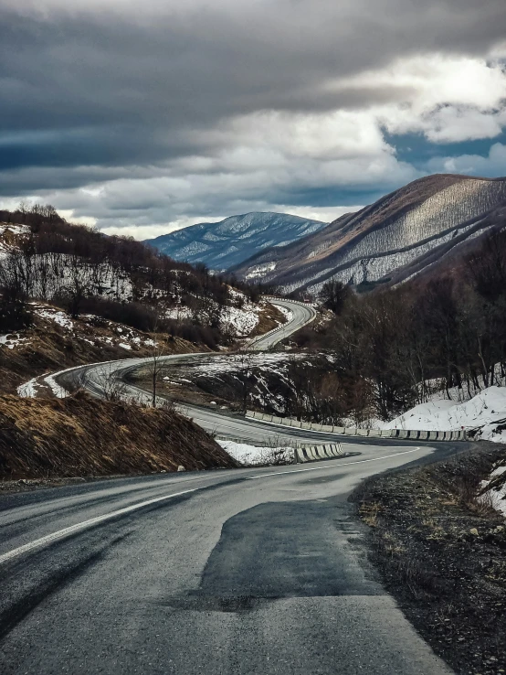 a scenic road in the middle of mountains under a cloudy sky