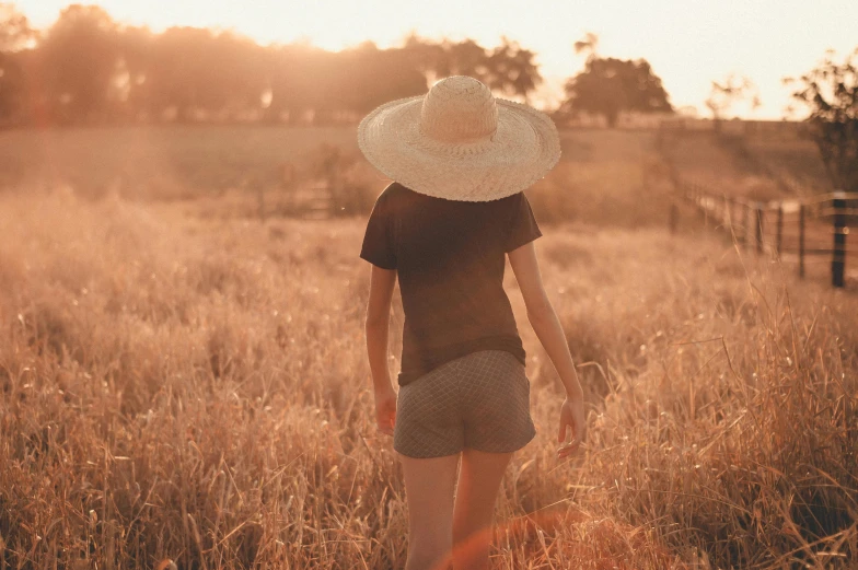 a woman in a hat walking through tall grass