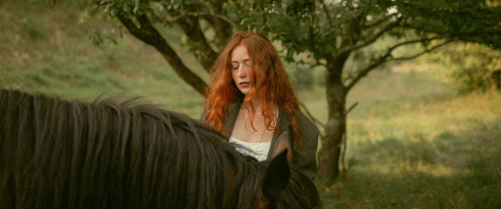 woman with red hair wearing a dress standing next to a horse