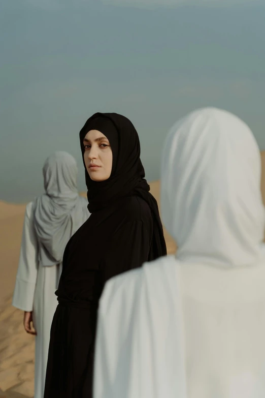 a group of women in white and black dresses walking across a sand field