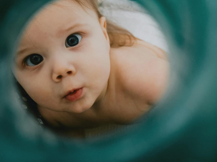 an adorable baby peering through the handle of a toy