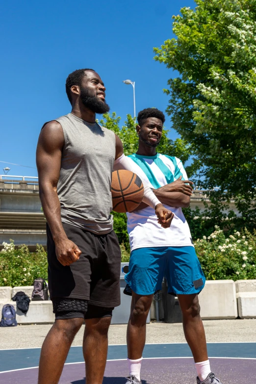 two men pose for a picture with a basketball on a court