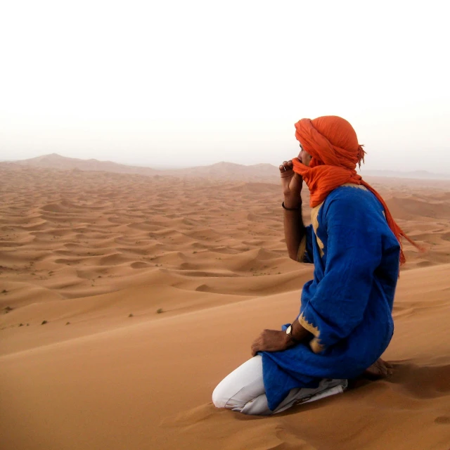 man sitting on a sand dune wearing orange head scarf