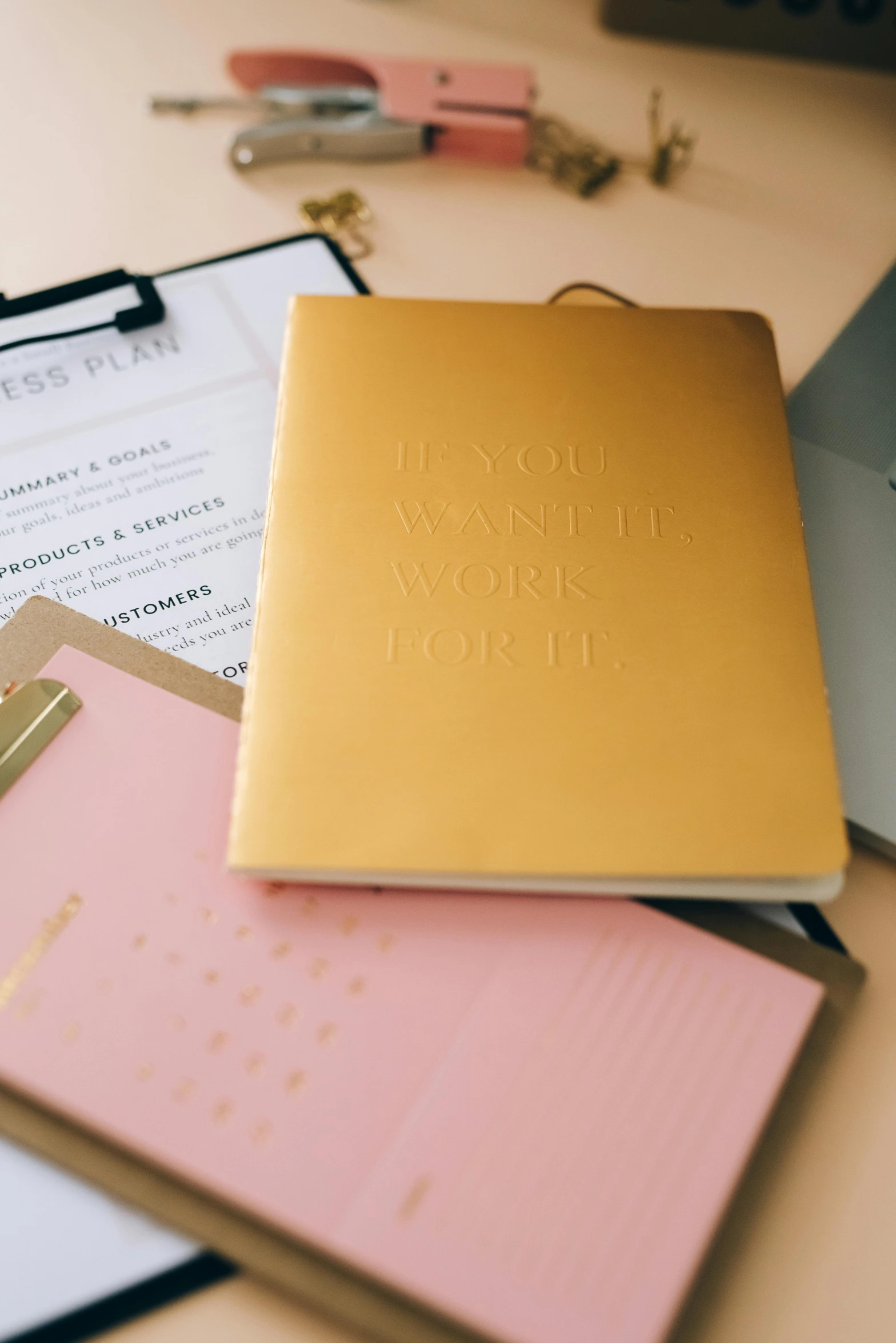 a small yellow notebook with a word on it sits in front of several pink and gold binders