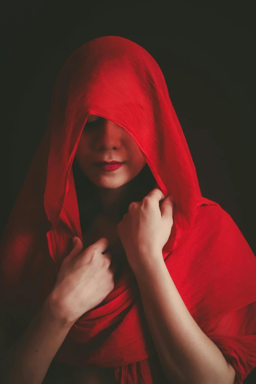 a woman in a red cloth covers her head with a hood