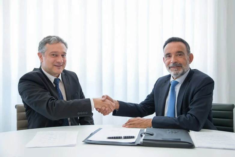 two men shaking hands while sitting at a table