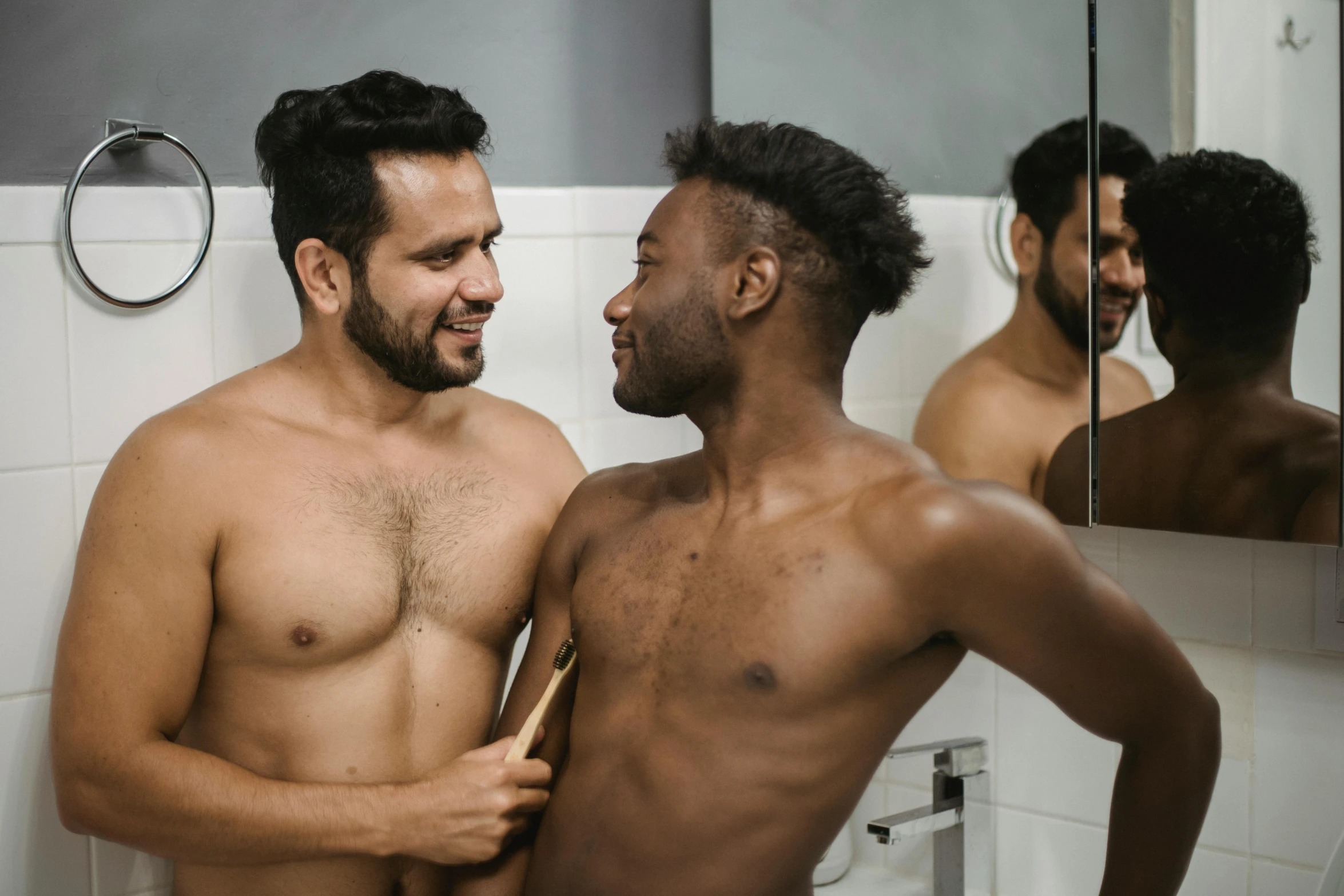 two young men, one without their shirt, are looking in the mirror