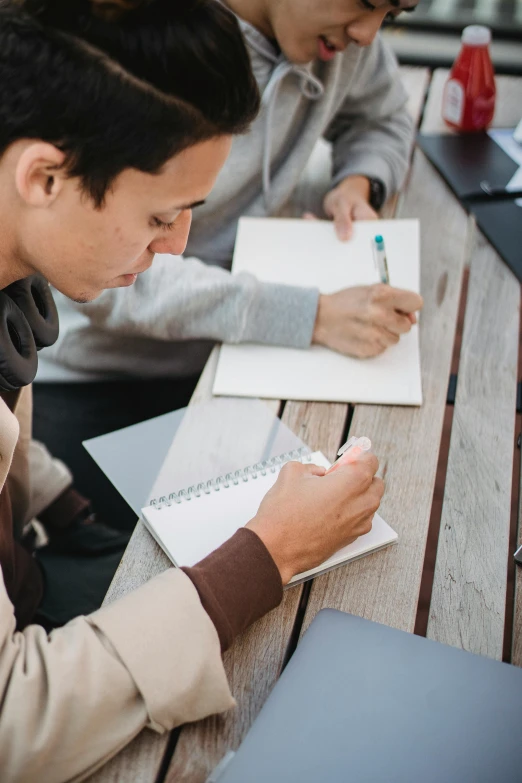 two men are taking notes while sitting at a picnic table