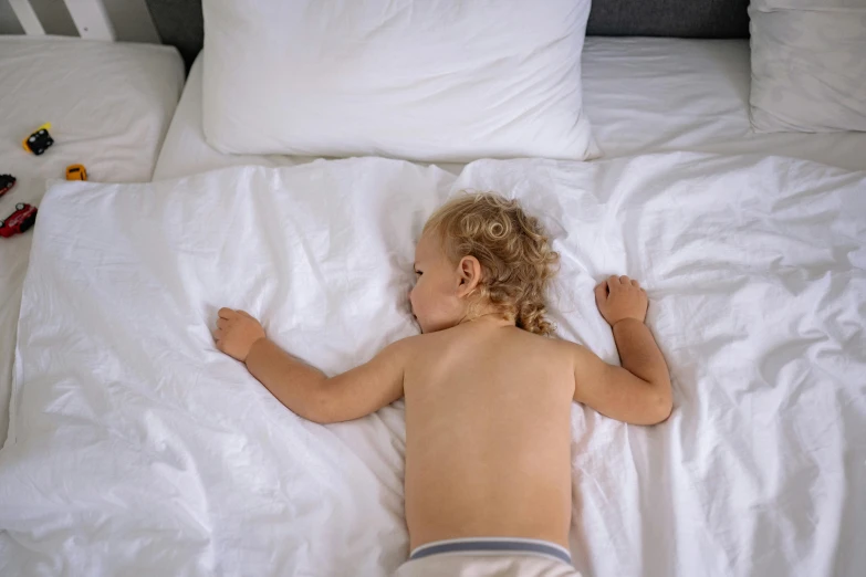 a child laying on top of a bed with white sheets