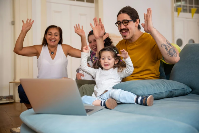 the family is in front of their laptop while the baby sits on top of the sofa