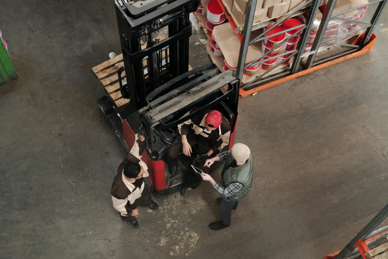 a small pair of workers talk with another man in front of some stacks of packages