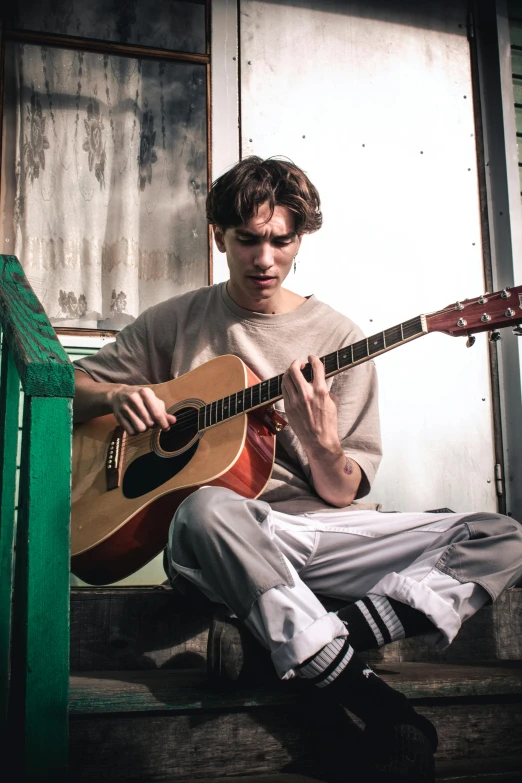 there is a man that is sitting on the stairs playing an acoustic guitar