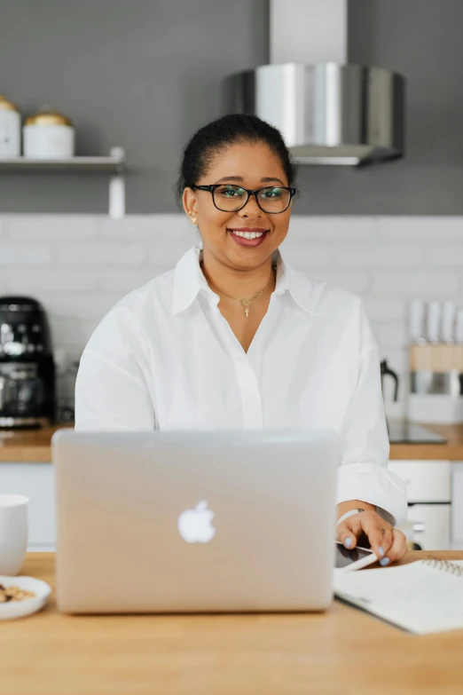 a woman smiling and working at a laptop on a kitchen counter