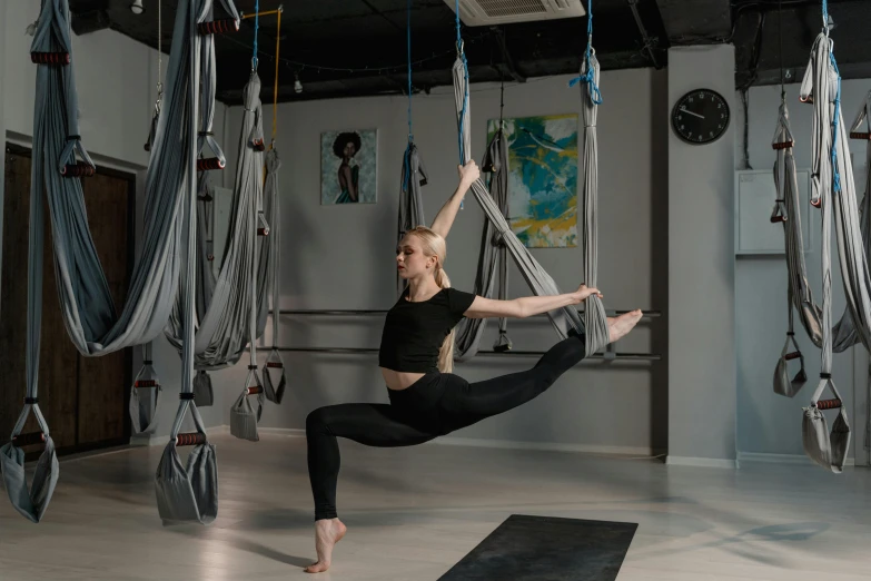 a woman doing aerial yoga in the middle of hanging gym equipment