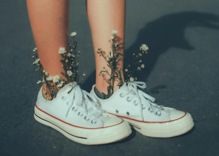 the feet and lowers of a woman wearing white sneakers with floraled lace