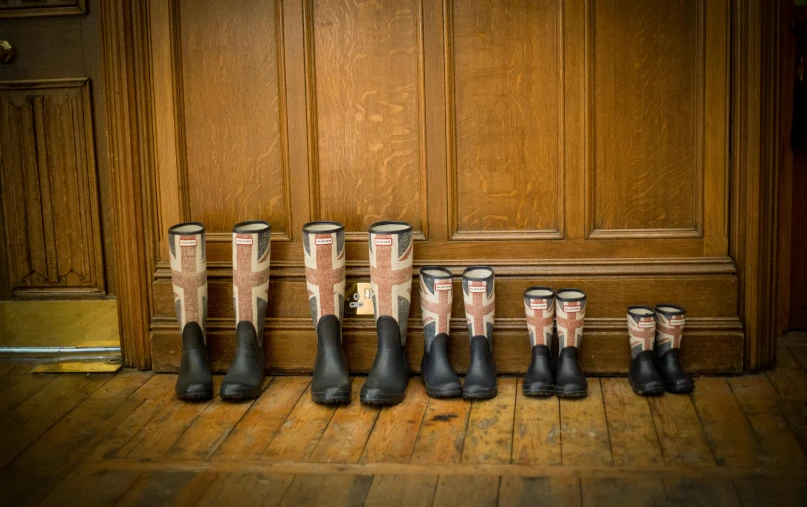seven black boots with patterned socks sitting in front of a wooden door