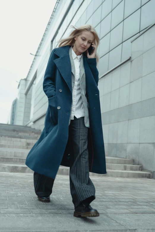 a woman in a long coat walks down some steps while talking on her cell phone