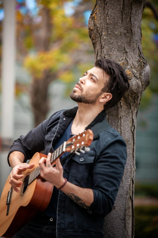 man playing guitar in front of tree, outdoors