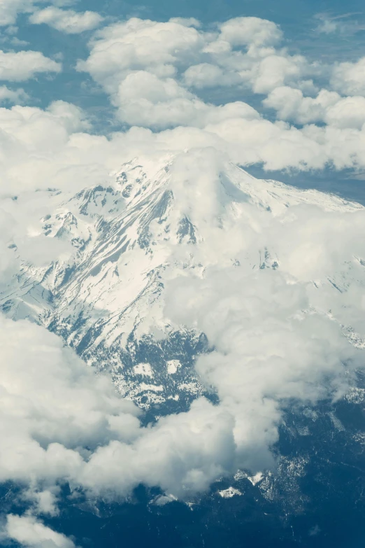 a mountain surrounded by some clouds with one snow - capped peak in the distance