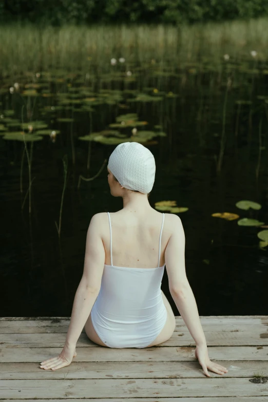 a woman in white sitting on a dock near water
