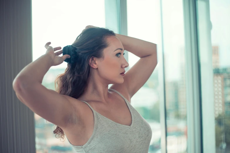 a woman standing near a window holding her hair