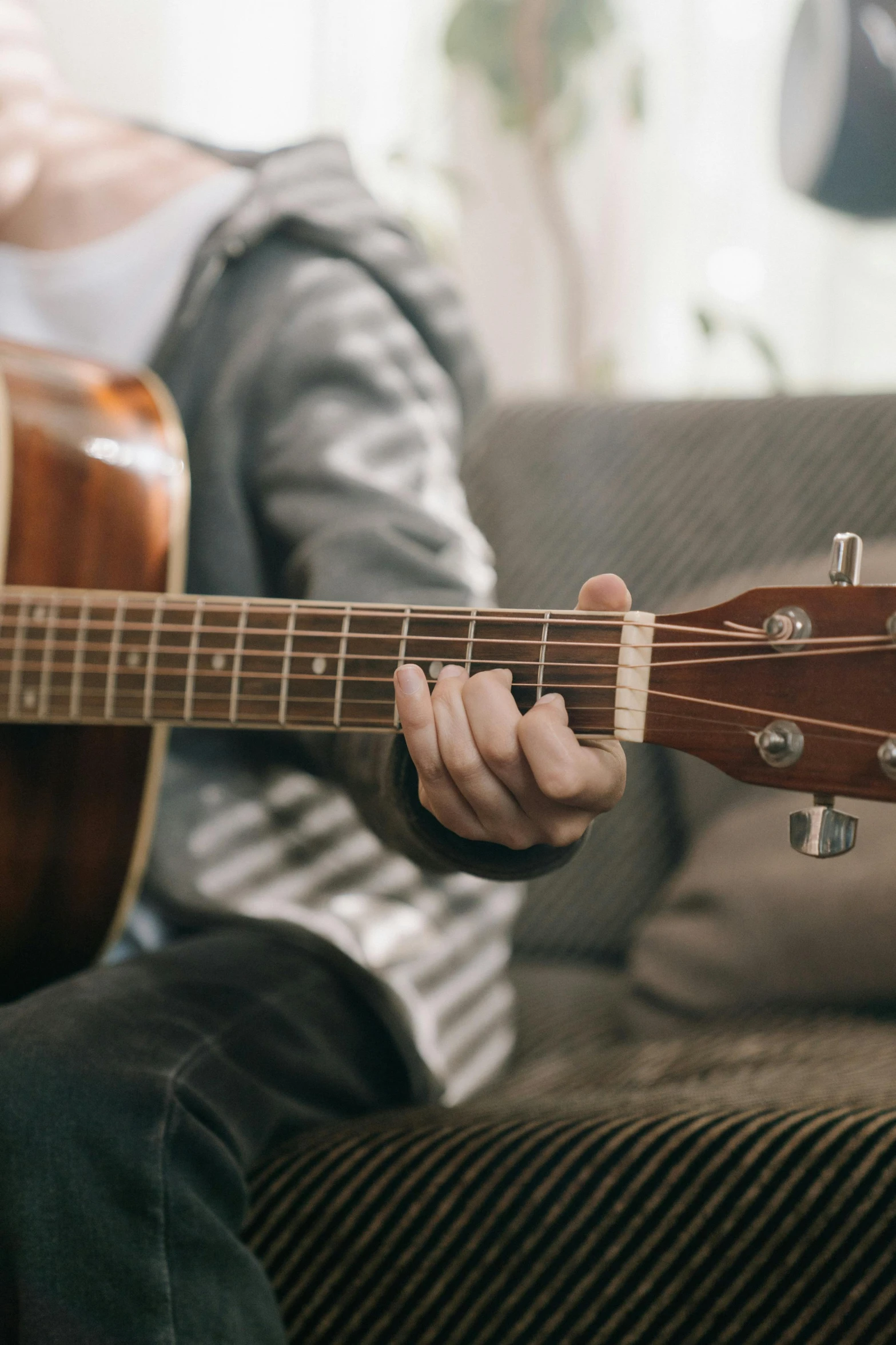 someone is sitting on a couch playing an acoustic guitar