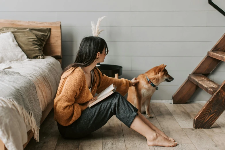 a woman reading a book with her dog on a hardwood floor