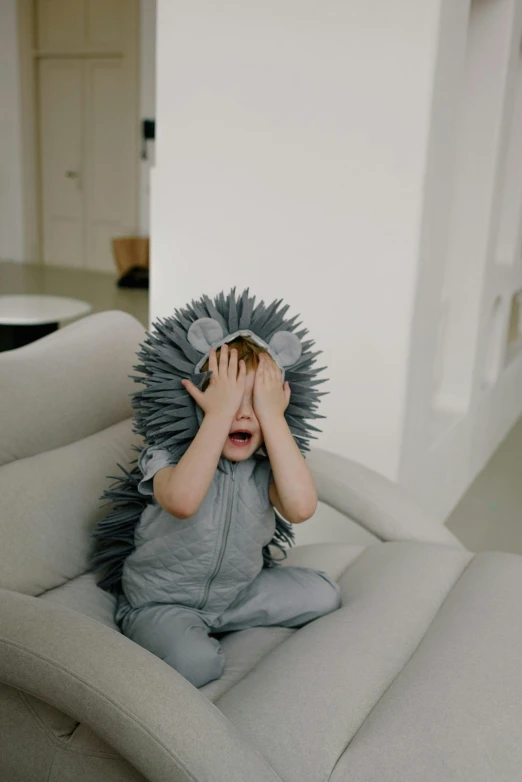 a small child is sitting in a chair covering his face with his hands