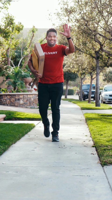 a man in a red shirt and black pants is holding a pizza box in the air