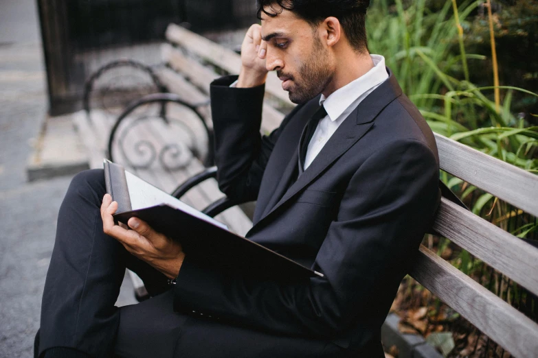 man reading book while sitting on park bench