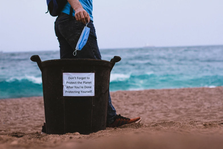 a man walking on the beach next to a trash can