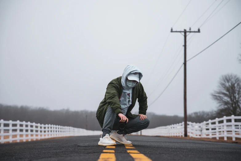 a person wearing hoodie crouches down on an empty road