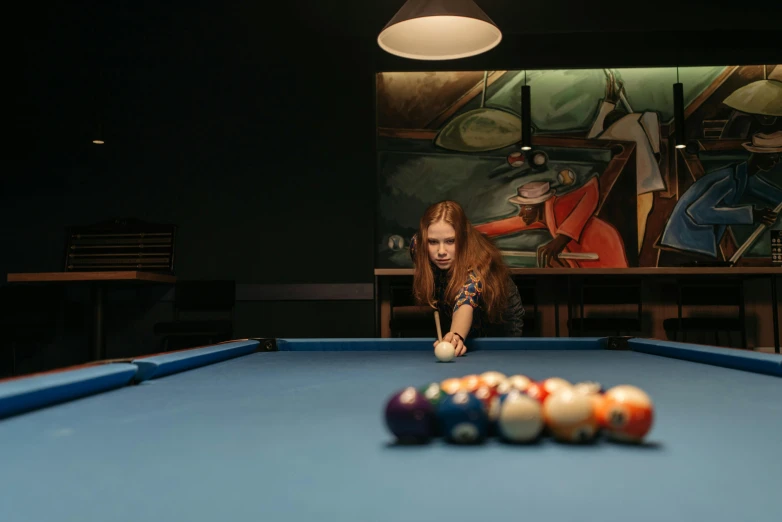 woman behind a pool table reaching towards a eight ball