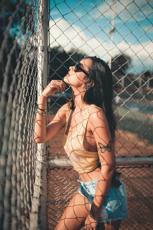 the woman with a tan tank top is leaning on a fence
