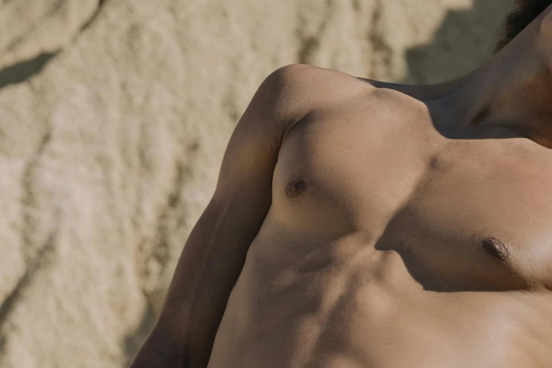 a close up of a man without a shirt laying on the beach