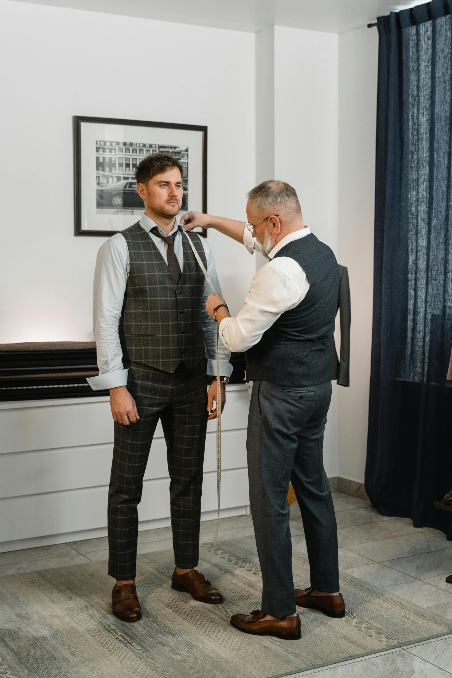 an older gentleman adjusts his neck tie as another man looks on