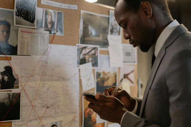 man in grey suit looking at cellphone on a corkboard