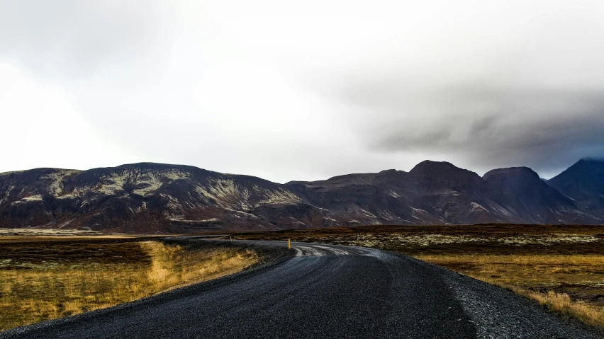 a single road with snow capped mountain peaks behind it