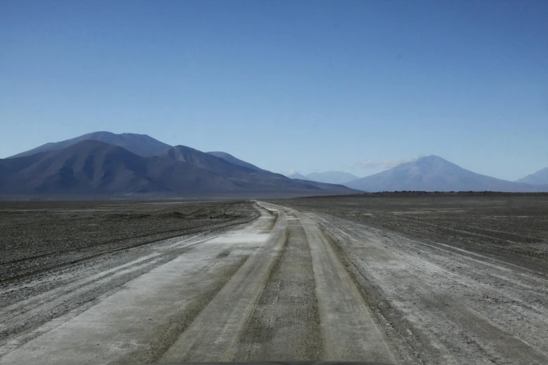 a dirt road on the edge of a desert with mountains in the background