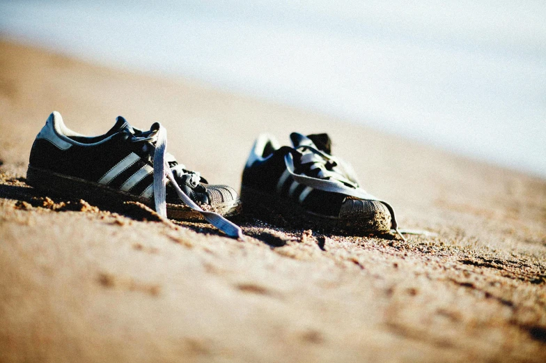 pair of tennis shoes on beach sand and water