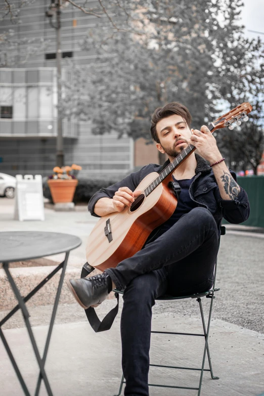 a man is sitting on a chair playing an acoustic guitar