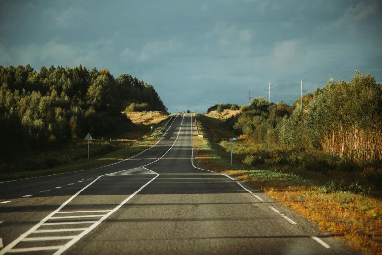 an empty road that is surrounded by grass and trees