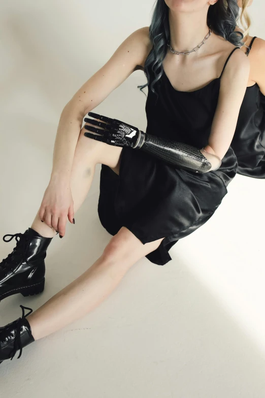 a woman in a black dress is sitting with a pair of boots