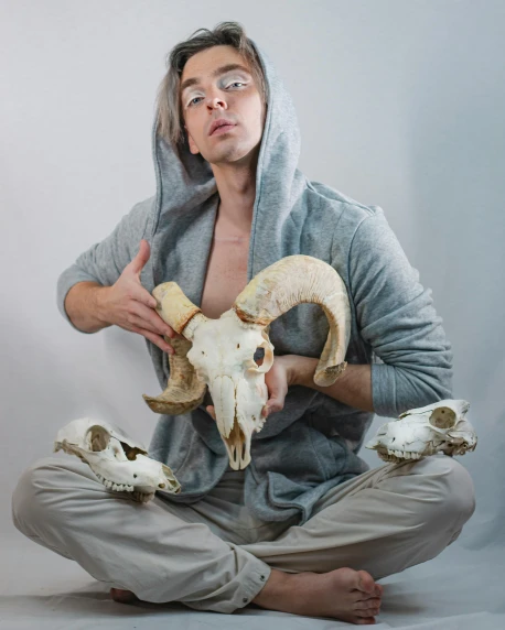 man in grey shirt sitting on the floor with goat skull masks