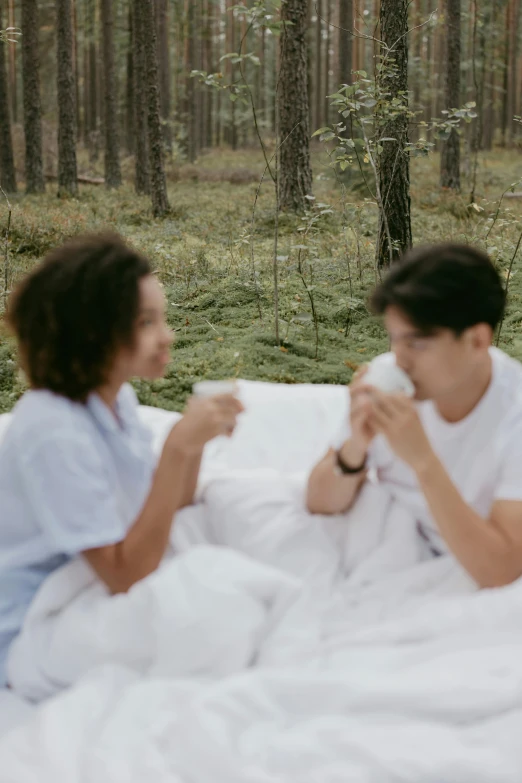 two people in white clothes are sitting under an umbrella in the woods