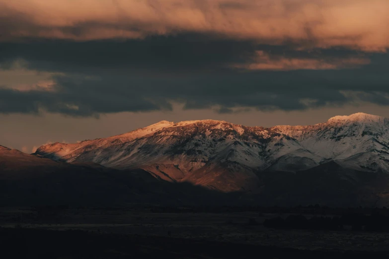 the white snow capped mountains are silhouetted against the cloudy sky