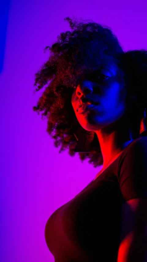 a girl with dark, curly hair posing for a picture in the pink and blue light