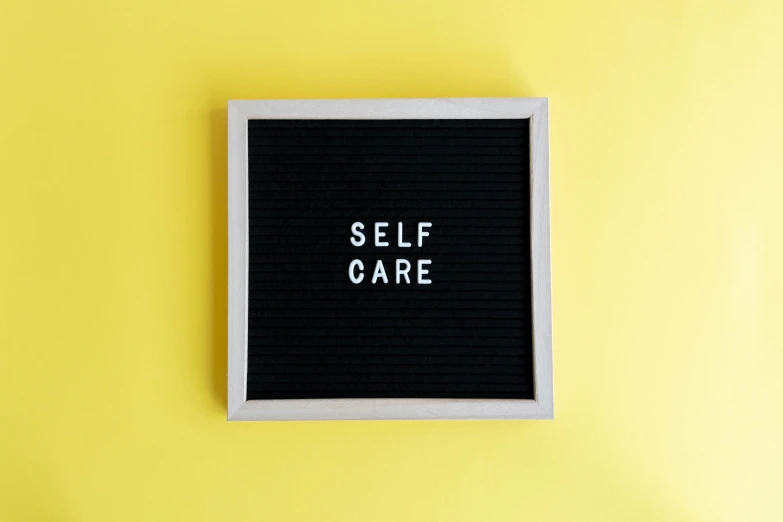 a black and white sign reading self care sitting on a yellow background