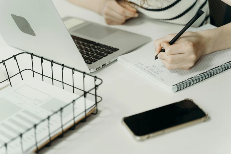 a person taking notes with a laptop and a cell phone