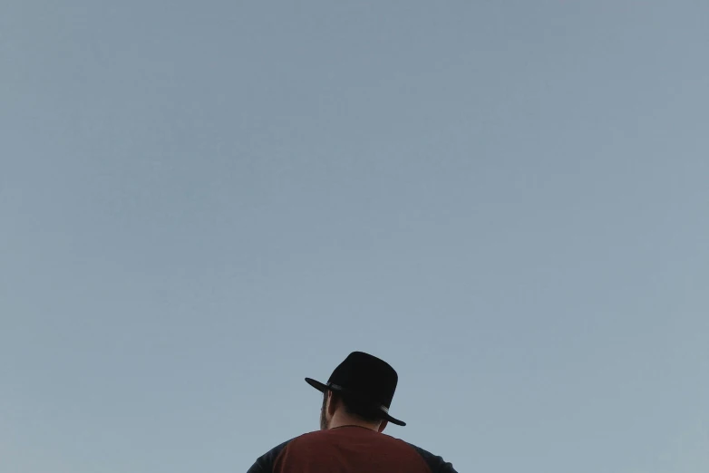 man wearing red shirt looking up at an airplane flying in the sky